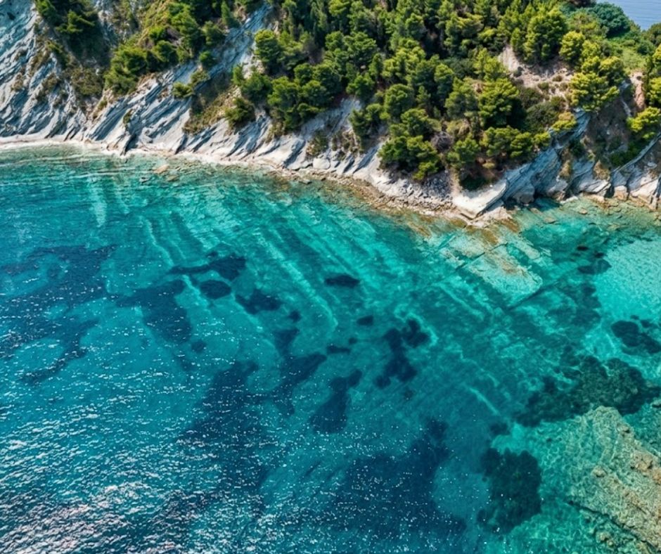 Sazan Island from the water, rocky coastline with old military structures and clear turquoise sea