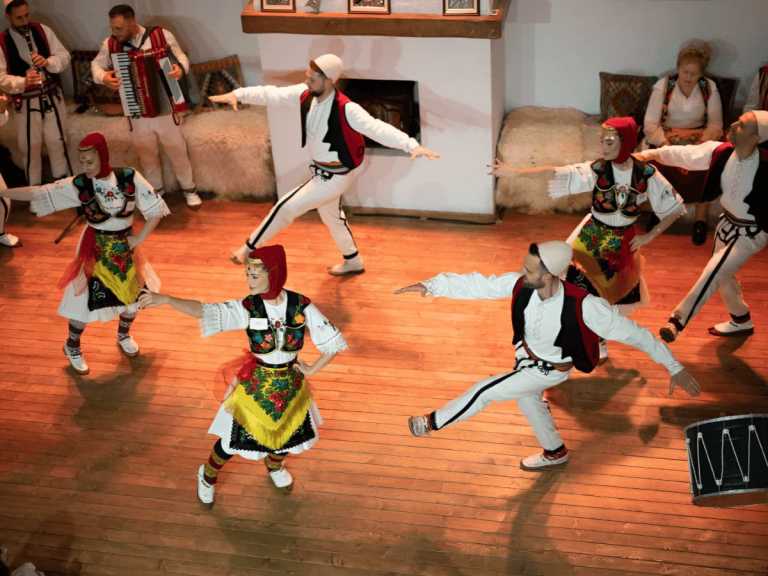 Dancers performing a traditional Albanian stick dance on a wooden floor at a folklore show in Tirana