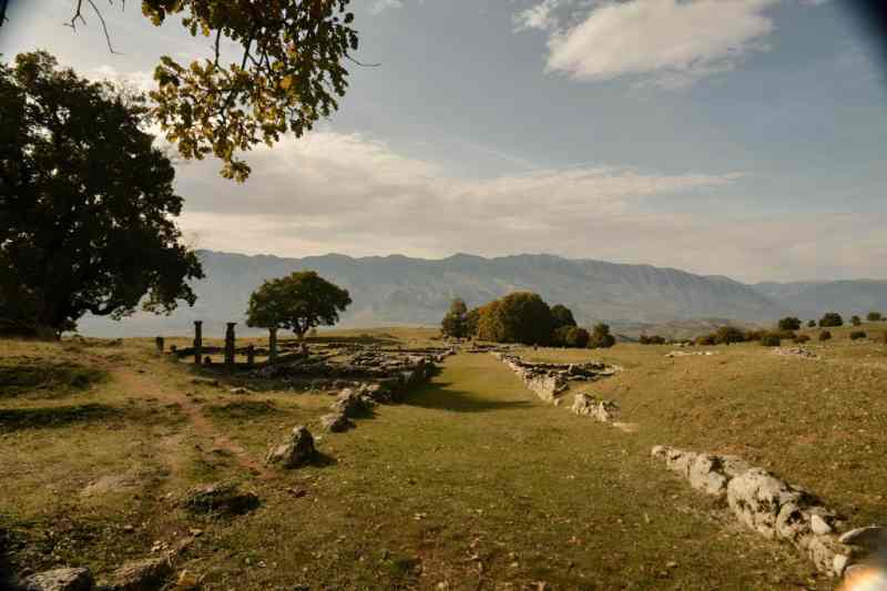 The ruins of the Antigonea Archaeological Park spread across a green hillside with mountain views near Gjirokastra