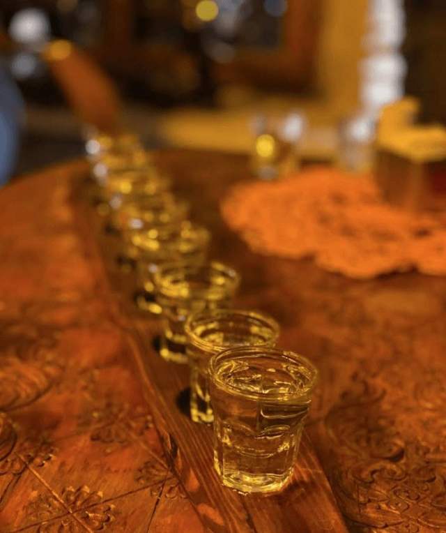 A row of raki glasses on a carved wooden table for a tasting in Berat