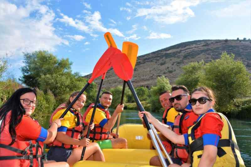 A group paddling a raft under a blue sky on the Bistrica River on a rafting day trip from Saranda
