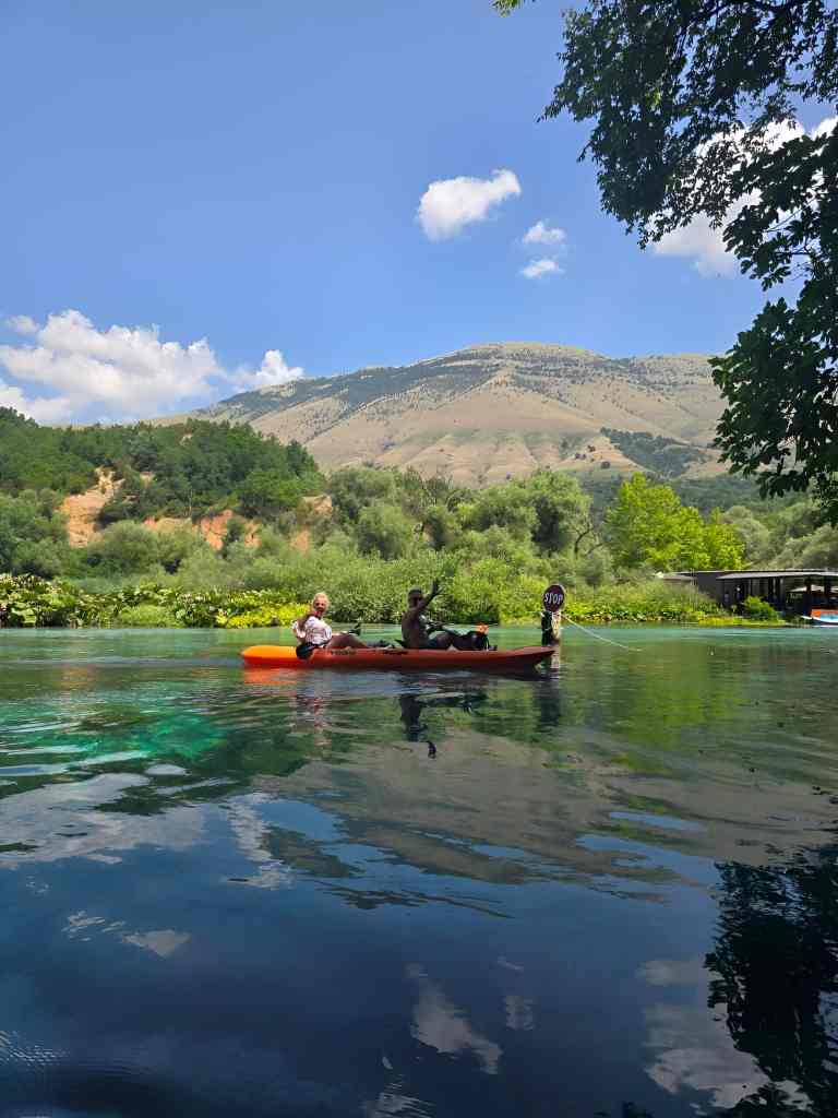 A red kayak on the calm Blue Eye water below green mountains