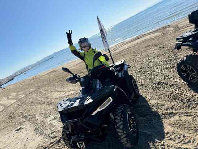 A rider on a quad bike on the beach at Cape of Rodon, arm raised