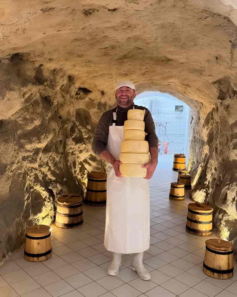 Man in an apron standing among large brass artillery shells in the cave arms museum at an ex-military base near Tirana