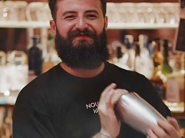Smiling bartender holding a cocktail shaker behind a bar in Tirana