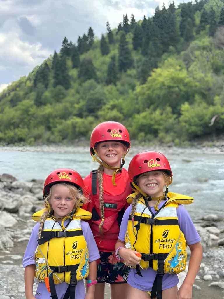 Two children in helmets and life jackets giving thumbs up beside the Vjosa River