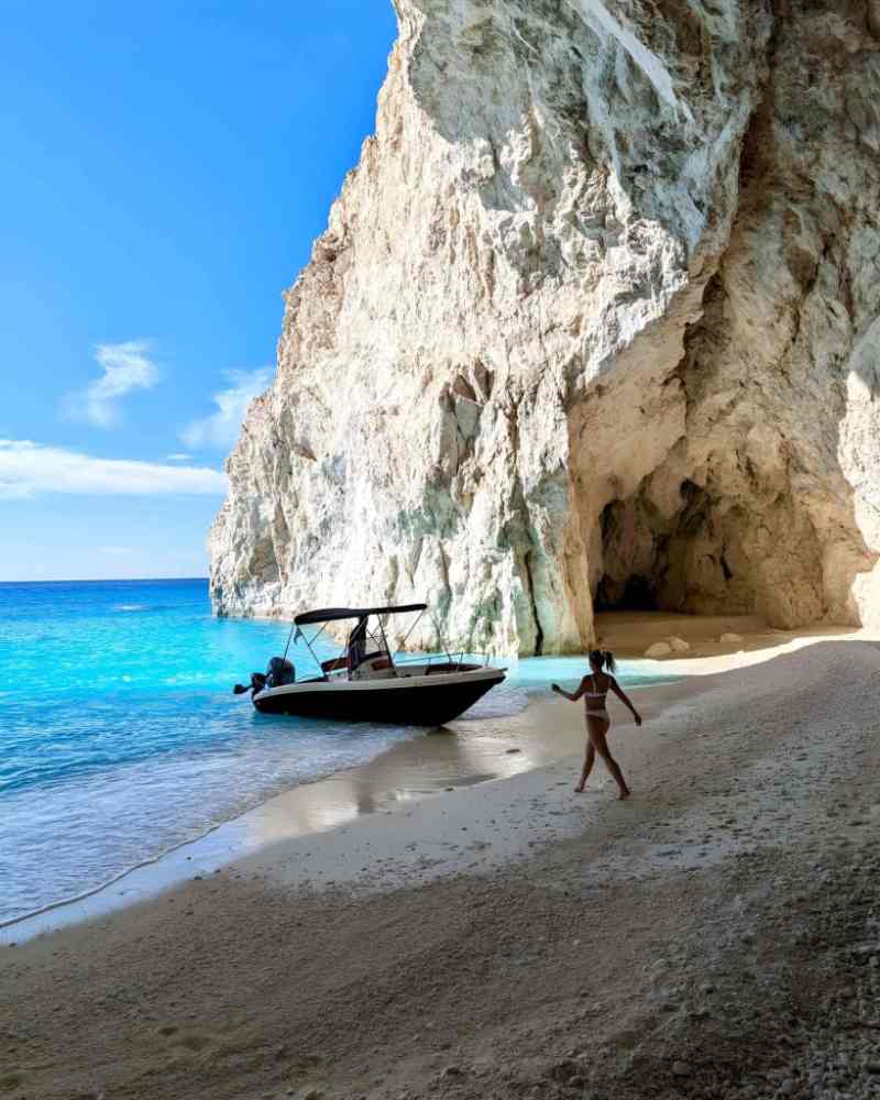 A boat on a hidden beach below tall white cliffs and sea caves on a Himara boat tour along the Ionian coast of Albania