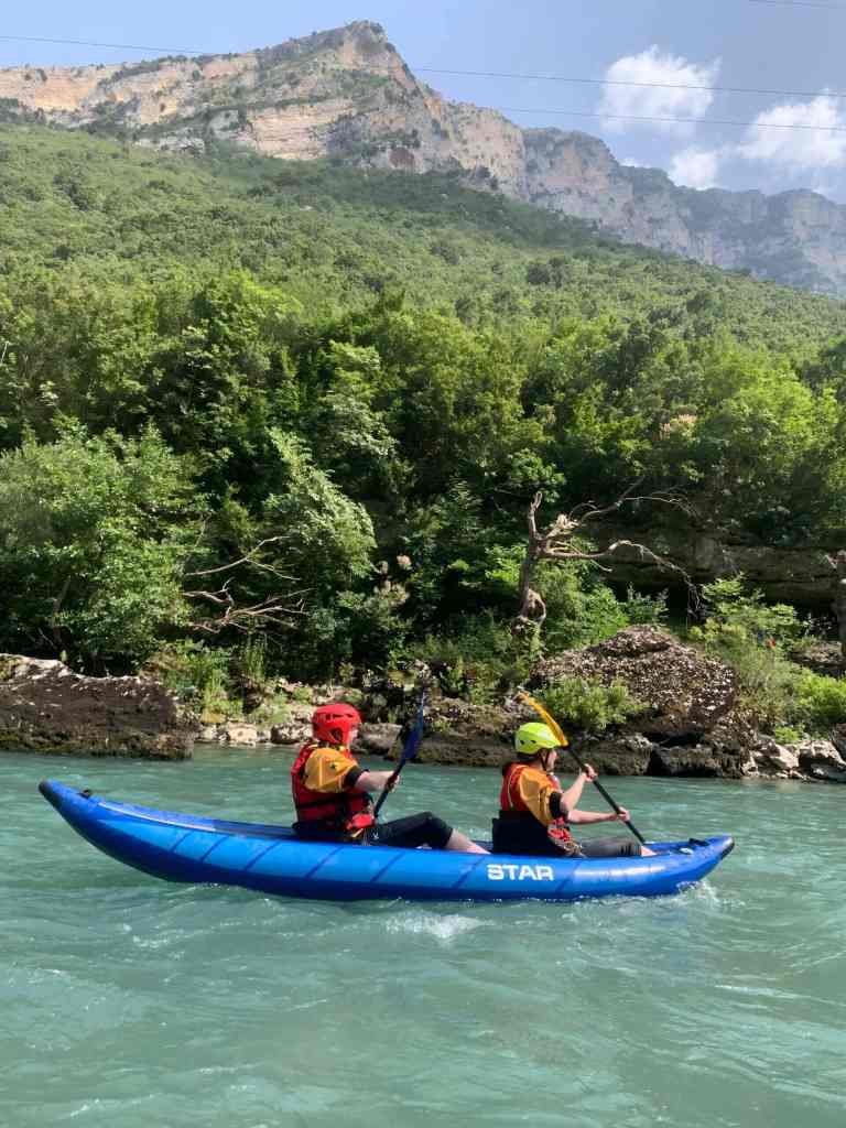 Kayakers paddling past green riverbanks on the Vjosa near Përmet