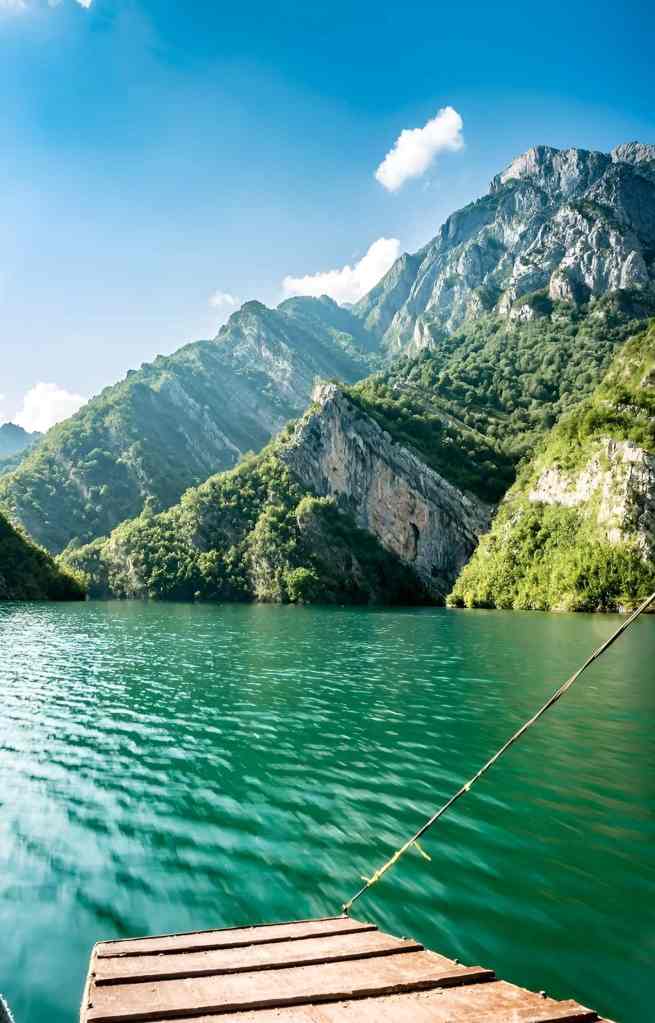 The green water and steep mountains of Koman Lake with a small wooden dock on a Koman Lake and Shala River day trip from Tirana