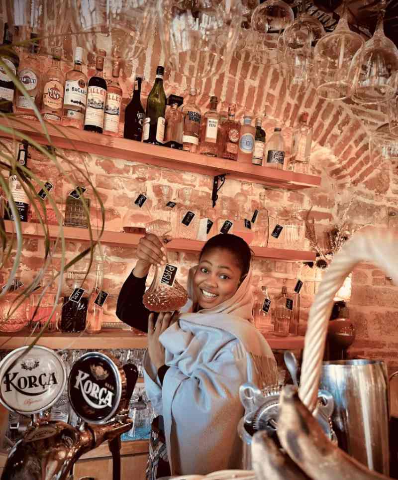 Smiling host pouring raki behind a bar in a traditional tavern in Korca