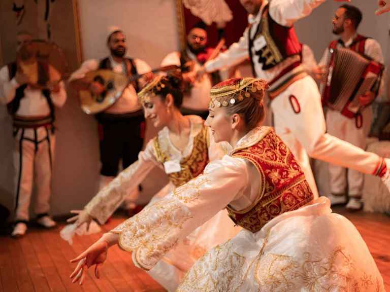 Albanian folk dancers performing beside a traditional musician at a night show in Tirana