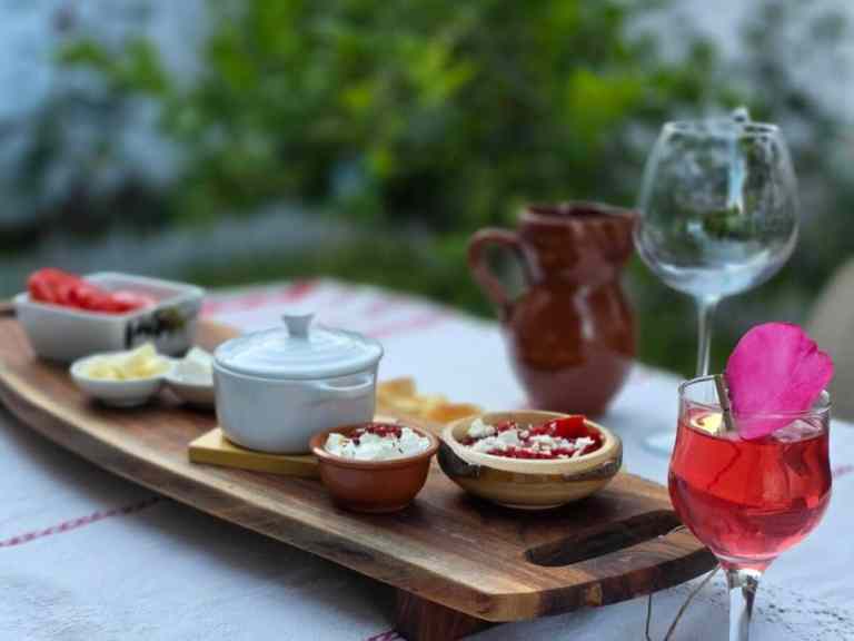 Wooden board with bowls of dips, a ceramic jug and a rose on a table in Shkodra