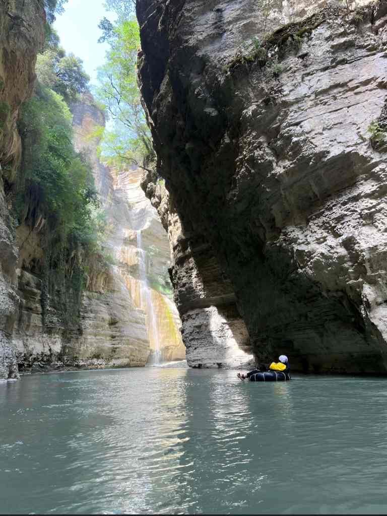 Person tubing on the green river between the tall walls of the Osum Canyon in Albania