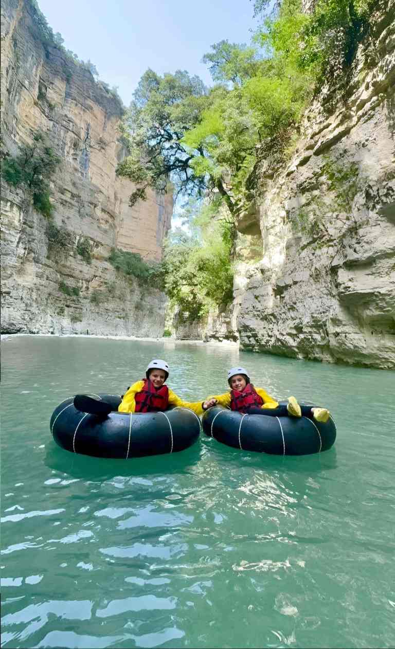 Two people floating on tubes in red life jackets on the green Osum Canyon river near Berat