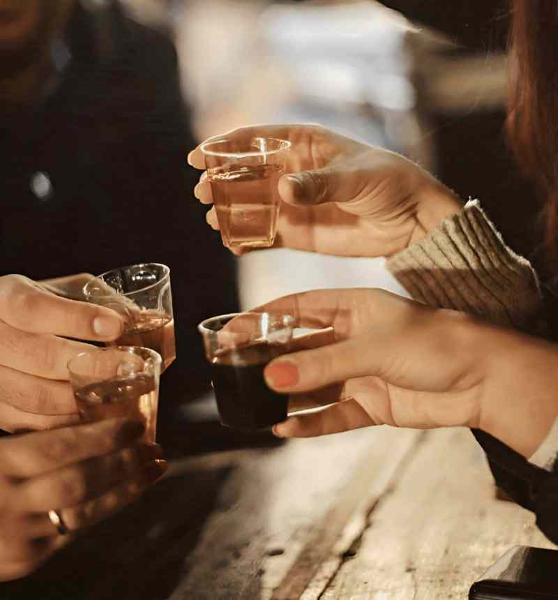 Hands toasting small glasses of raki at a tasting in Korca