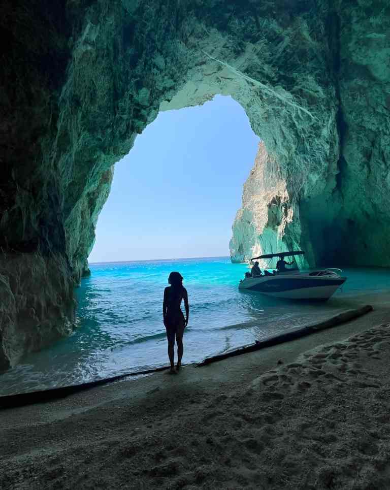 A boat inside a blue sea cave with a person on the sand on a Saranda boat tour along the Ionian coast of Albania
