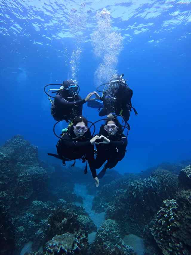 Group of scuba divers swimming above a rocky reef in clear blue water near Saranda, Albania