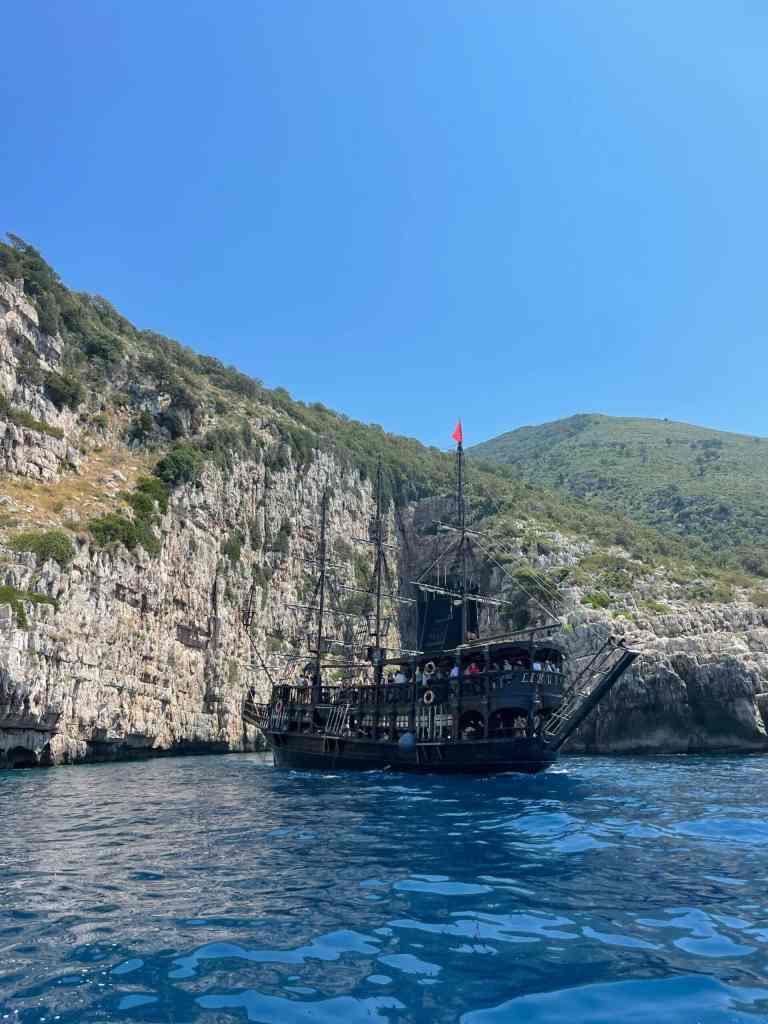The wooden tour boat approaching a sea cave in the rocky cliffs of the Karaburun Peninsula near Vlora