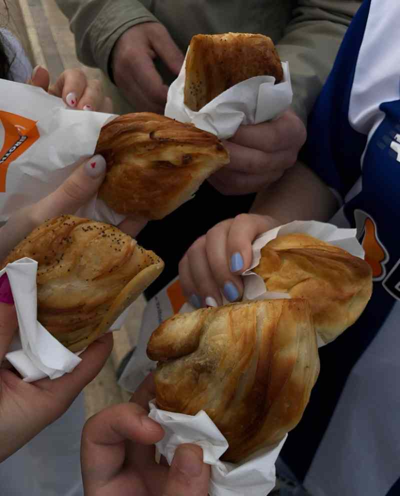 Hands holding byrek pastries in paper on a Tirana street food tour