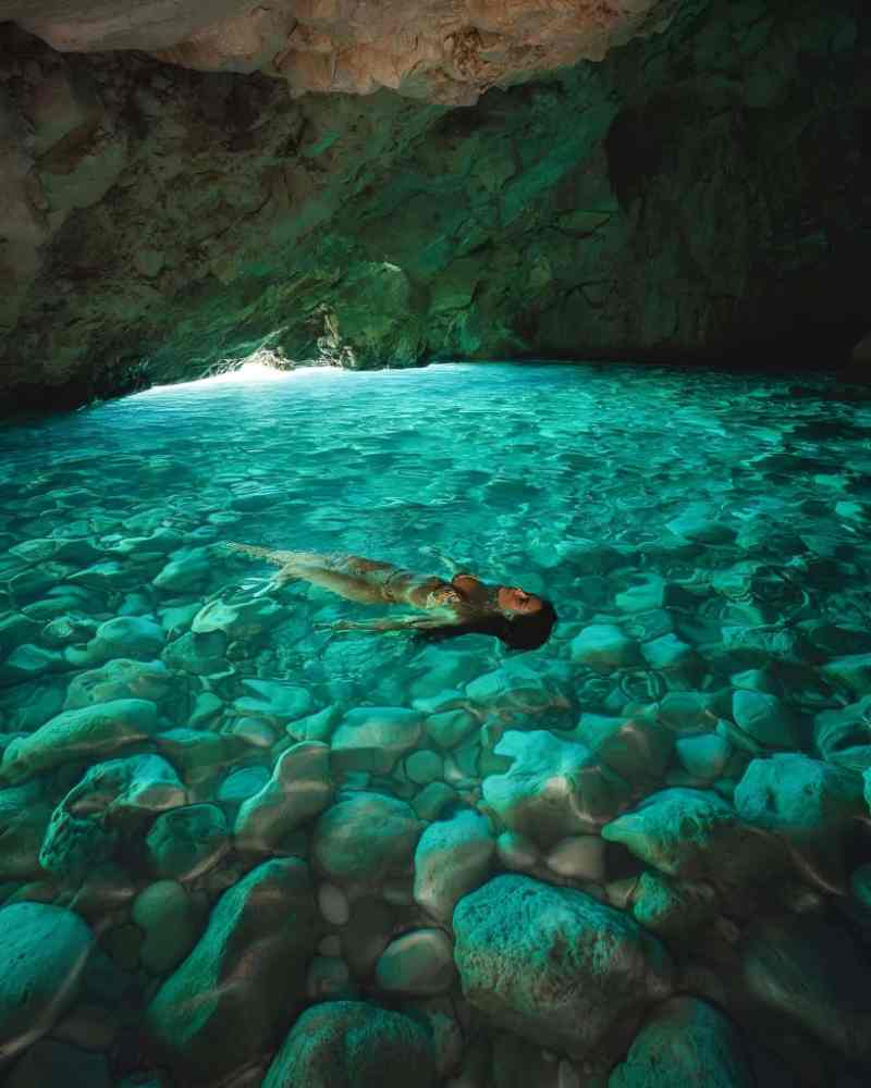 A snorkeller swimming over rocks in the clear turquoise water of a sea cave on a Himara boat tour, Albania