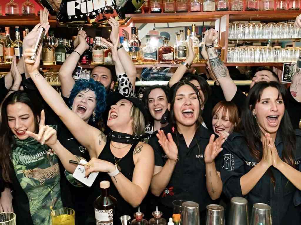 Group of young people cheering with arms raised at a busy bar during a Tirana pub crawl