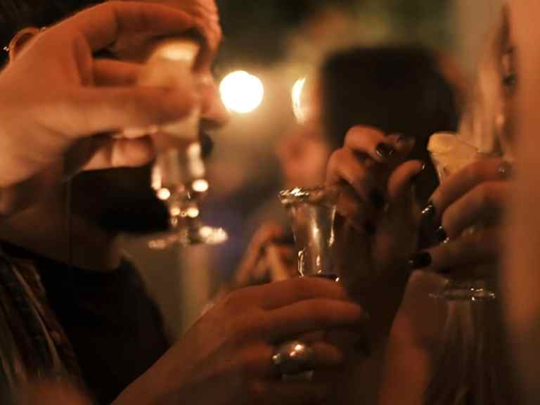 Hands toasting small shot glasses under warm light during a Tirana pub crawl