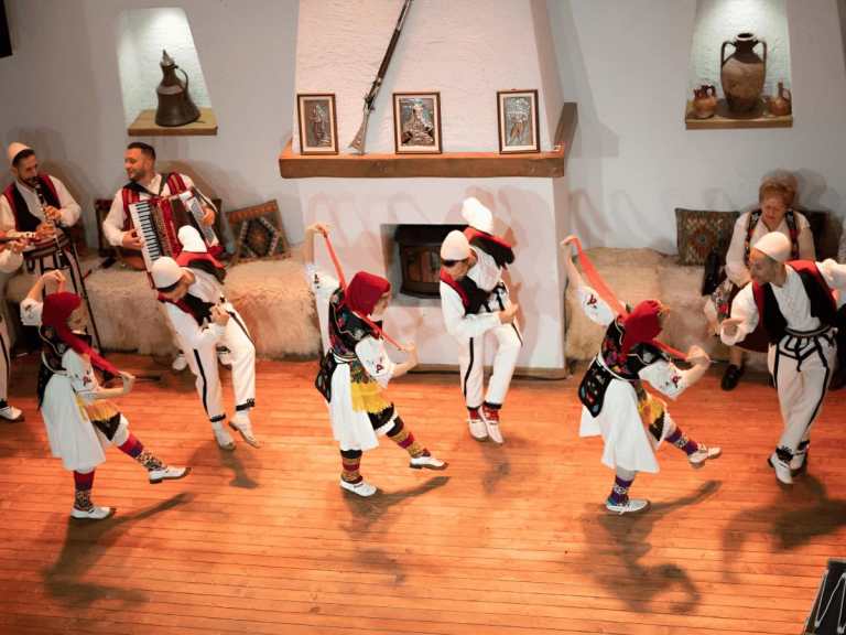 Group of dancers in white traditional costumes dancing in a circle at an Albanian folklore show