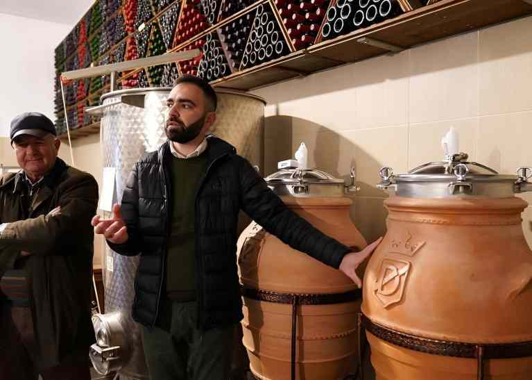 Man standing beside large traditional clay wine amphoras in an Albanian winery