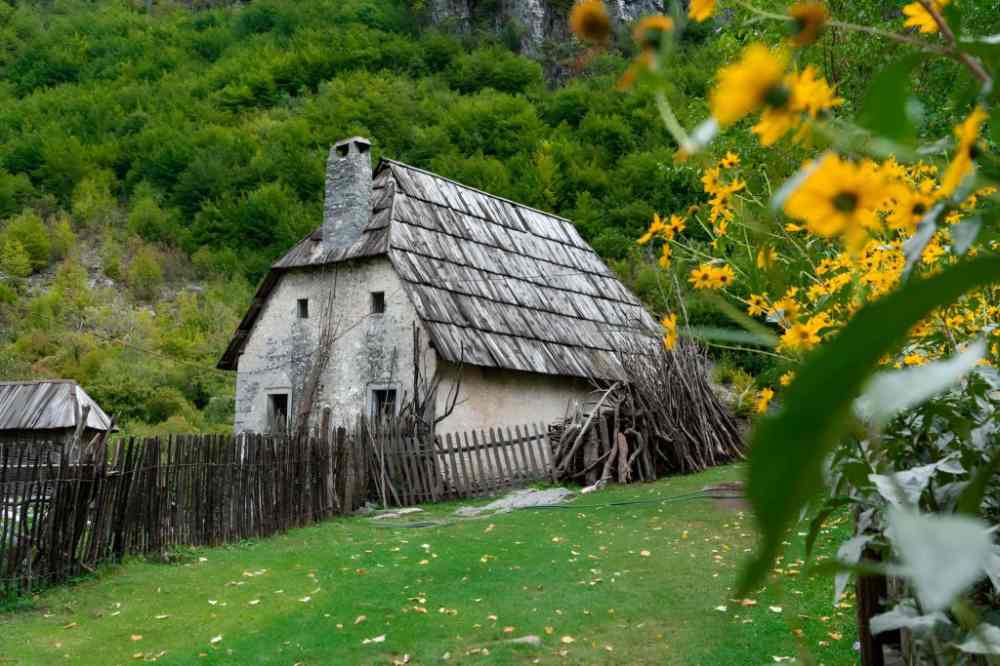 A traditional stone house with a shingle roof and sunflowers in Theth village in the Albanian Alps