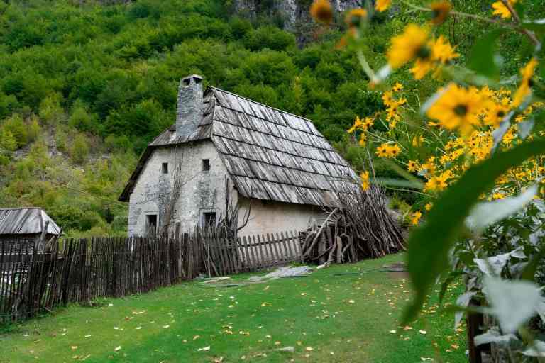 A traditional stone house with a shingle roof and sunflowers in Theth village in the Albanian Alps