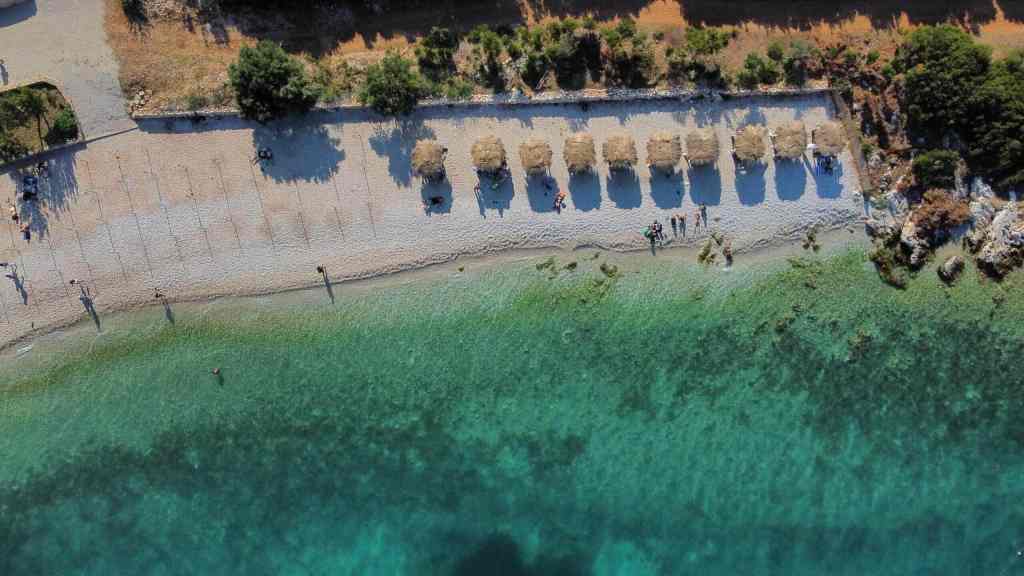 A quiet turquoise bay with sun loungers seen from the water on a Vlora boat tour along the Ionian coast