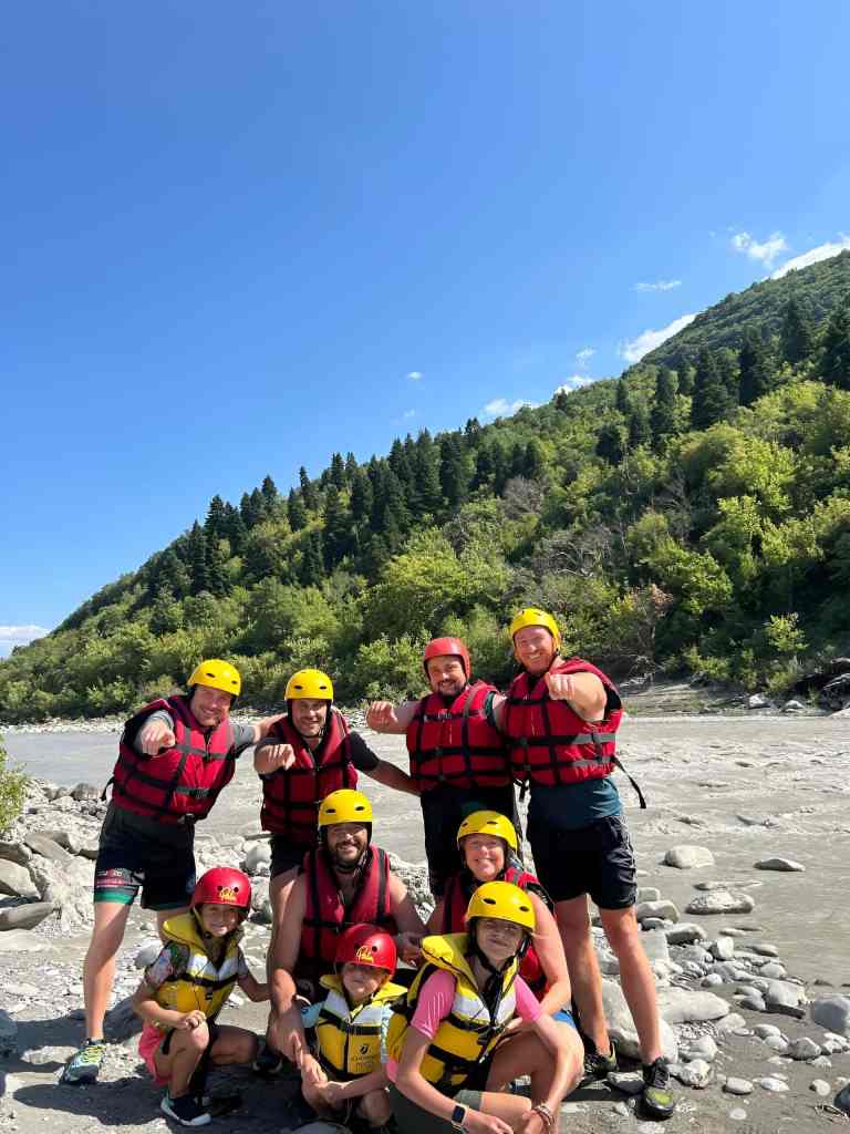 Group of rafters in life jackets posing on the bank of the Vjosa River with mountains behind