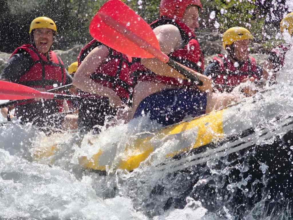 Group paddling a raft through white-water rapids with splashing water on the Vjosa River in Albania