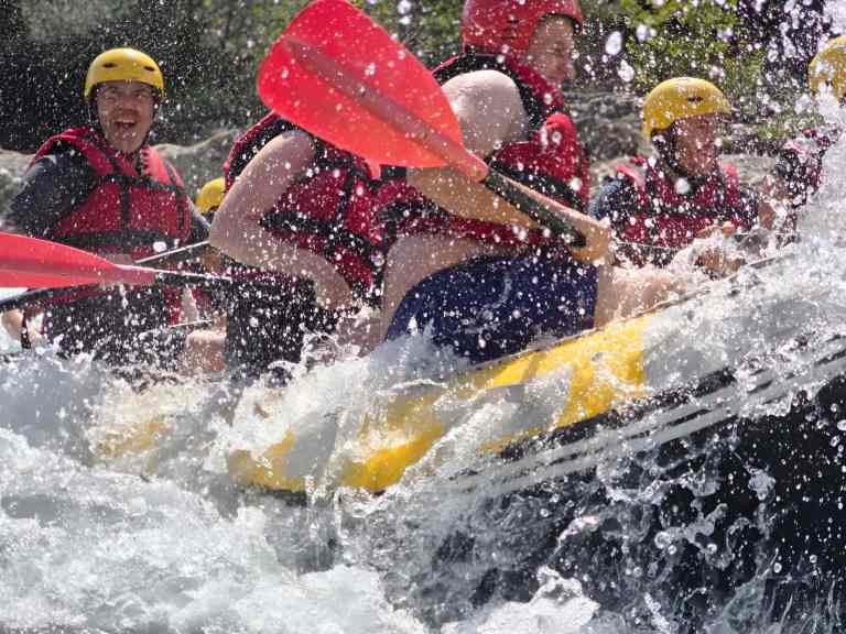 Group paddling a raft through white-water rapids with splashing water on the Vjosa River in Albania