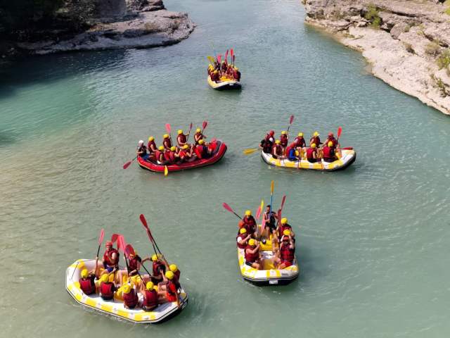 Several rafts floating on the turquoise Vjosa River between green hills near Gjirokastra