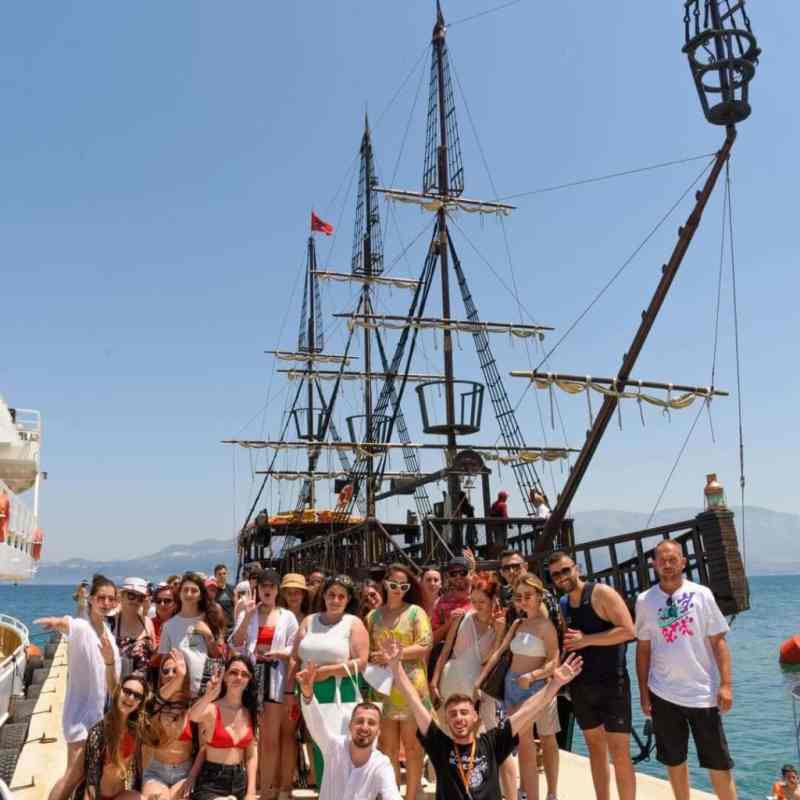 Guests sitting along the wooden deck under the flags of the pirate-style boat on a Vlora boat tour to Sazan Island and Karaburun
