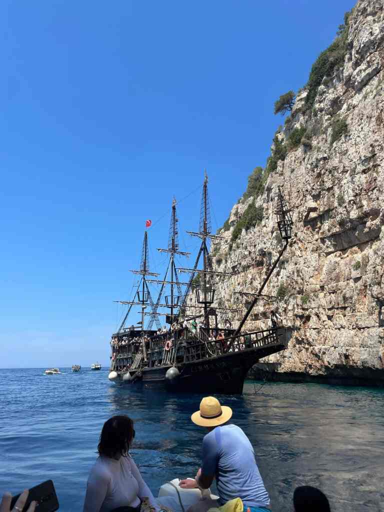 A wooden pirate-style tour boat sailing past tall white cliffs on the Ionian coast during a Vlora boat tour to Sazan Island and the Karaburun Peninsula