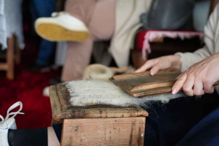 Hands working raw wool on a wooden board in Lazarat