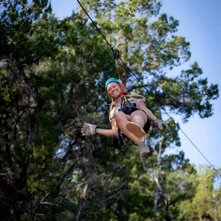 Person in a blue helmet ziplining over green forest near Tirana