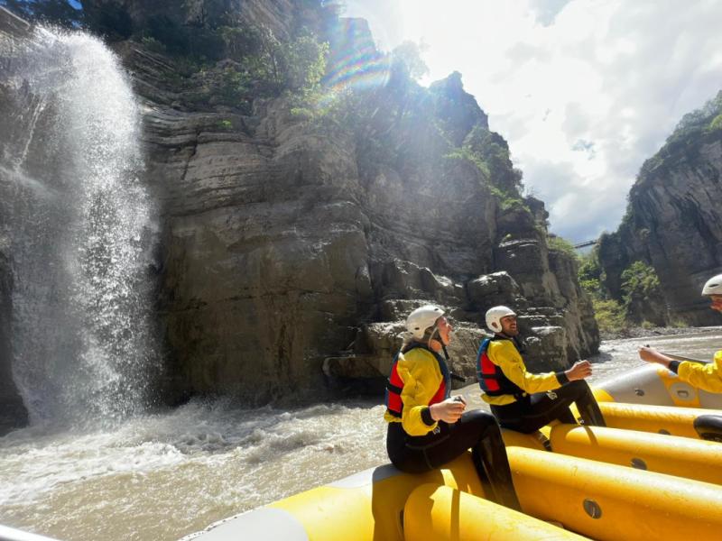 Yellow raft passing a waterfall in Osum Canyon, Albania, with local rafting guides in helmets and life jackets