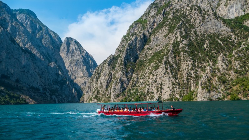 Red passenger speedboat crossing Koman Lake between limestone cliffs, part of the Shala River day trip from Shkodra