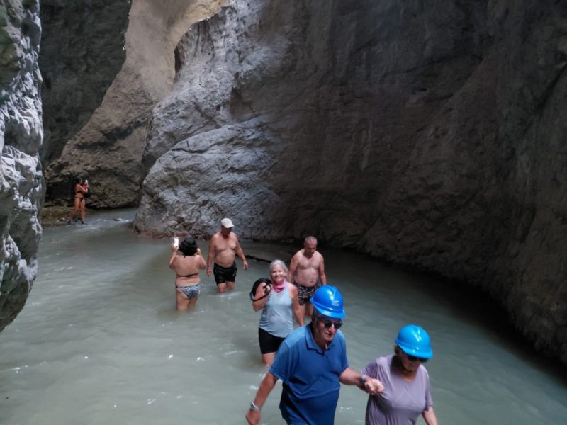 Hikers in helmets wading through the milky water of Holta Canyon, Albania